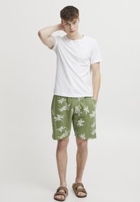 Green shorts with white floral pattern, lightweight fabric, elastic waistband, paired with a plain white t-shirt and brown sandals.