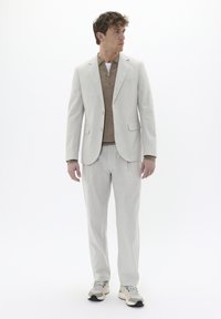 Traje gris claro con blazer de un solo botón, suéter beige con cremallera por debajo y pantalones a juego, combinado con zapatillas beige.