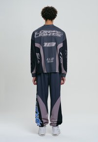 Cămașă sport cu mâneci lungi și pantaloni în gri închis, cu accente gri deschis și bleu, având grafice mari pe spate și pe laterale.