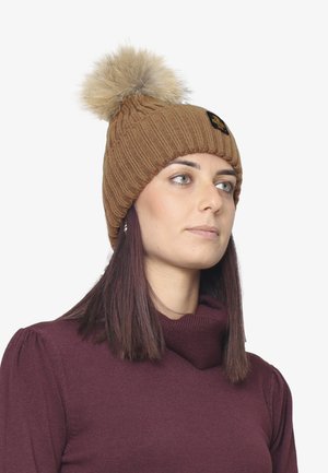 Beanie lavorata a maglia marrone con motivo a coste e un pompon in pelliccia sintetica beige sopra. Presenta un piccolo logo nero sul davanti.