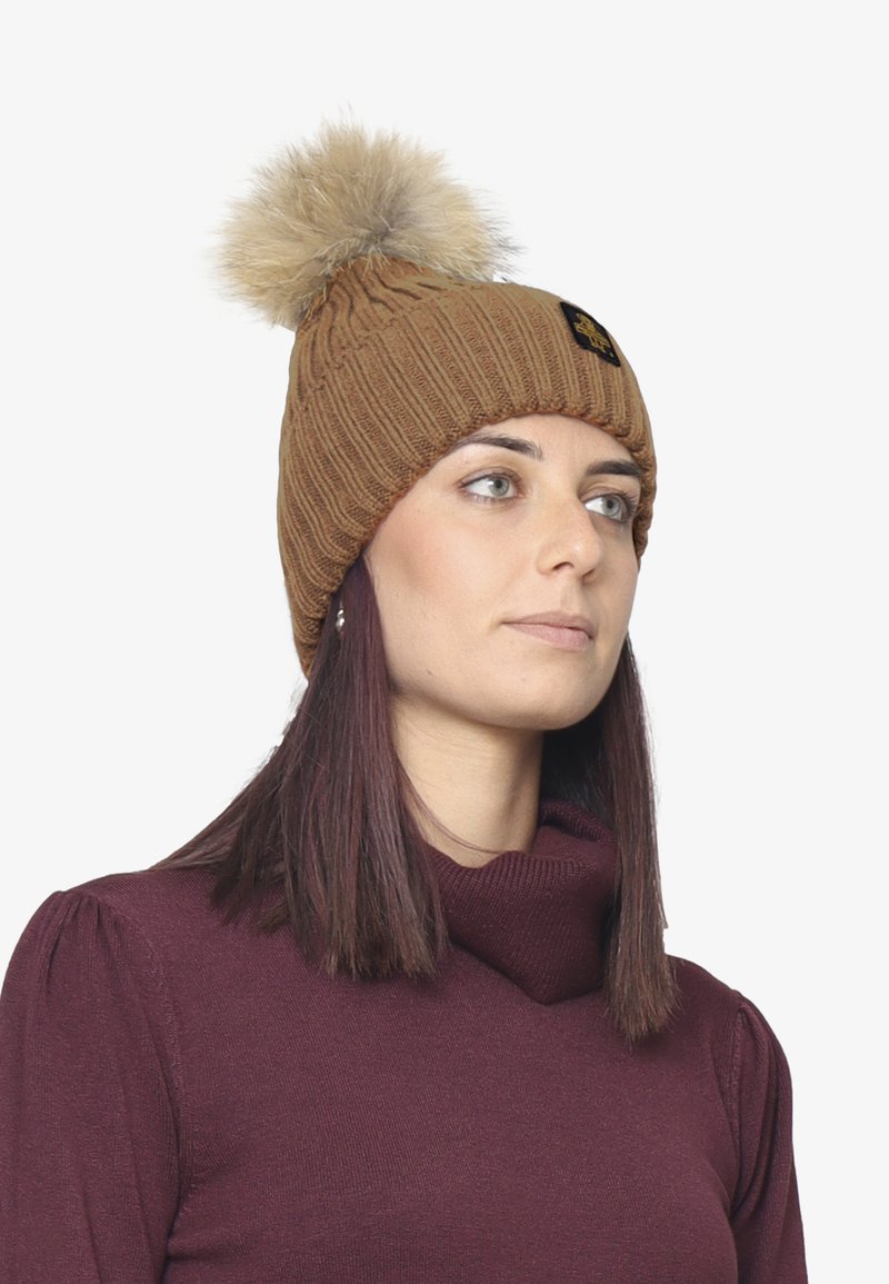Beanie lavorata a maglia marrone con motivo a coste e un pompon in pelliccia sintetica beige sopra. Presenta un piccolo logo nero sul davanti.