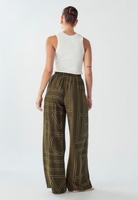 Zelene široke hlače s uzorkom i elastičnom gumom u struku, s bijelim geometrijskim linijama. U kombinaciji s pripijenom bijelom rebrastom majicom bez rukava.