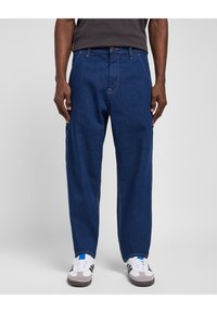 Blue denim jeans with a straight-leg design, featuring visible stitching and pockets; paired with white and gray sneakers with blue accents.