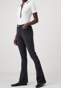 White ribbed polo shirt with a black trim, paired with dark wash flared jeans. Slim fit with classic button flies and pockets. Black flat shoes.
