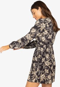 Vestido negro de flores con mangas largas abullonadas, cintura elástica y patrón de flores doradas. Tejido ligero y diseño hasta la rodilla.