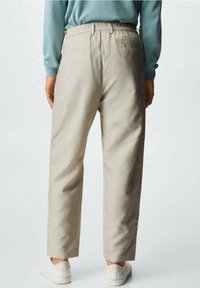 Lichtbeige katoenen broek met een elastische tailleband, rechte pijpen en twee achterzakken. Draagt met witte sneakers.
