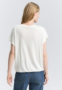 Haut blanc à manches courtes en tissu doux, avec une coupe décontractée et un col rond, associé à un jean en denim bleu.