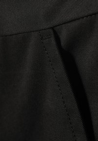 Tela negra con una textura lisa, que presenta costuras ajustadas y sutiles patrones de tejido diagonal. Primer plano de una sección de una prenda estructurada.