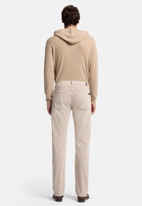 Felpa color sabbia con cappuccio regolabile abbinata a jeans dritti beige chiaro. Texture liscia, design minimalista, tasche standard.