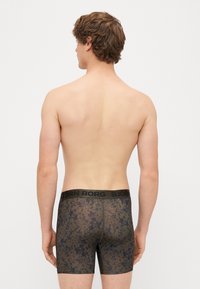 Mustmust ja tumedate mustritega bokserid, mis on kontrastse logo vööga, valmistatud läbipaistvast ja elastsed materjalist, sobiv disain.