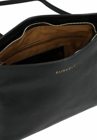 Borsa in pelle nera con dettagli in oro sulla cerniera. L'interno è rifinito con una fodera in tessuto beige e presenta una tasca ulteriore con cerniera per riporre gli oggetti.