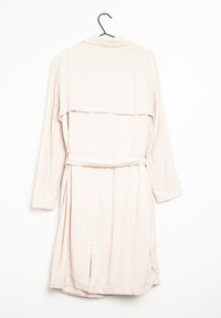 Bata de manga larga rosa claro con cuello, cinturón en la cintura y aberturas laterales, hecha de una tela suave. Cuélga de un gancho negro sobre un fondo blanco.
