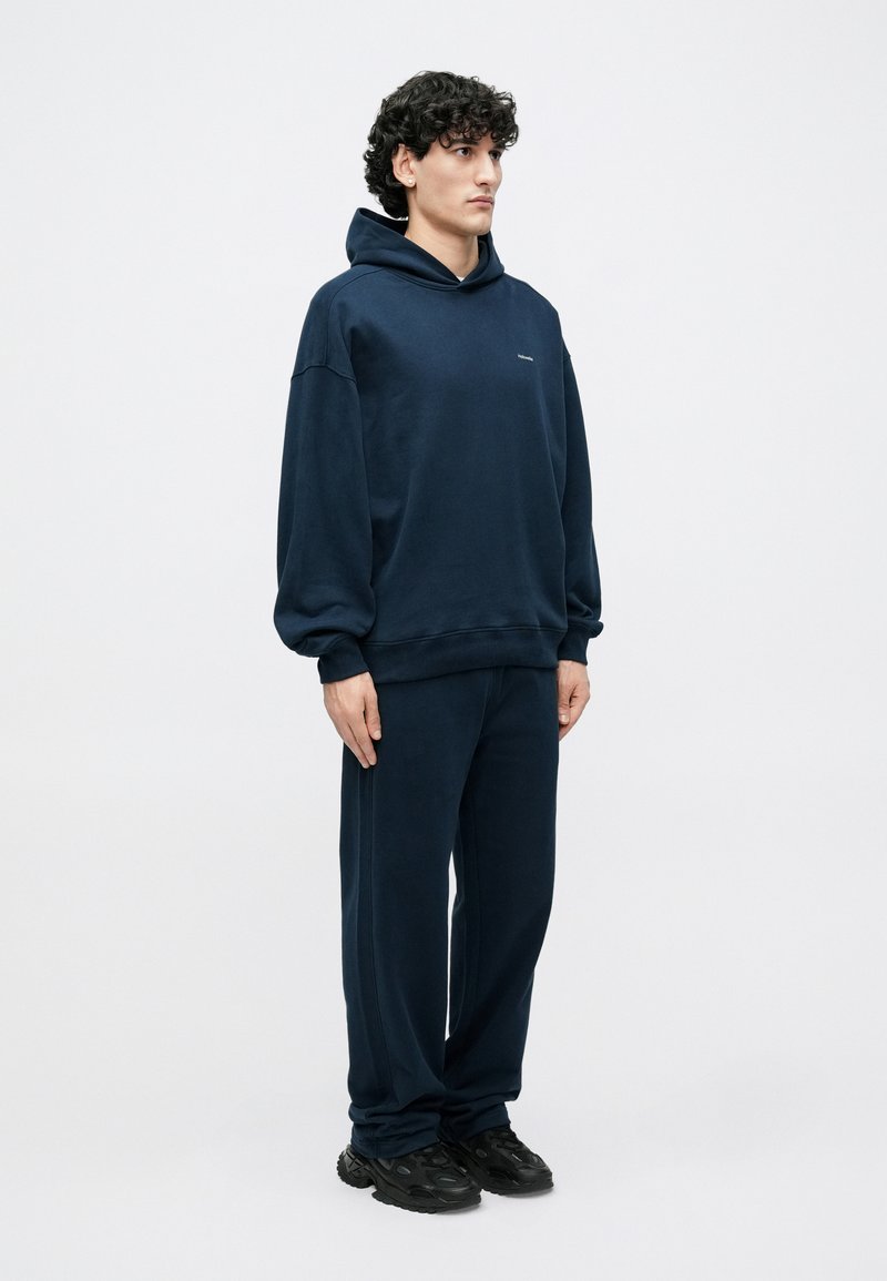 Navy blue hoodie and matching sweatpants in a soft fabric. The hoodie features a relaxed fit and a front pocket, with minimal branding.