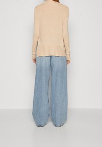 Pull tricot beige avec un col rond, associé à un pantalon en denim bleu à jambes larges. Le tissu semble doux avec une coupe décontractée.