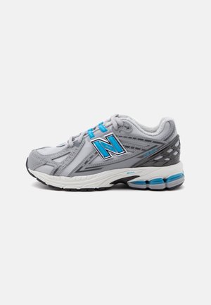 Grå og hvid New Balance løbesko med blå accenter, tyk polstret sål og logo på siden, vist fra ydersiden.