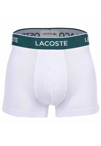 Vita bomullboxershorts med ett grönt elastiskt midjeband som har "LACOSTE"-logotypen. Slät textur och åtsittande form, inga mönster eller accenter.