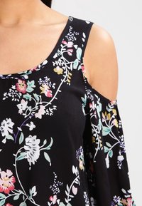 Blusa nera floreale con design a spalle scoperte, motivi floreali colorati, tessuto morbido e scollatura rotonda con maniche svolazzanti.