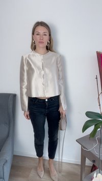 Casaco cropped em seda na cor bege claro, com decote redondo e fecho de botão na frente, combinado com jeans pretos ajustados e sapatos de salto nude.