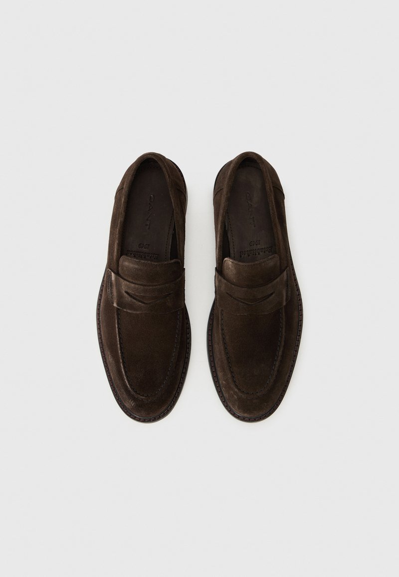 Mocassins en daim marron avec un design de style mocassin, comportant des détails de couture et un accent surélevé subtil sur le dessus. Semelles plates.