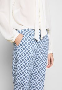 Pantalon bleu et blanc à motif losange ; tissu léger, coupe droite, poches latérales, associé à un chemisier clair.