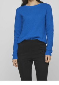 Blå stickad tröja med en texturerad design, rund halsringning och ribbad mudd, ihop med svarta åtsittande byxor.