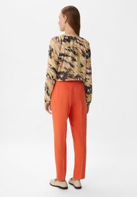 Krótka, wielokolorowa bluzka w kamuflażowy wzór; zestawiona z pomarańczowymi spodniami typu tapered; modelka w beżowych slip-onach.