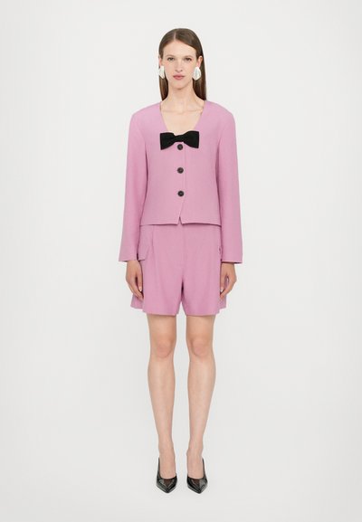Lavender-colored suit featuring a boxy blazer with a black bow detail and three black buttons, paired with tailored shorts.
