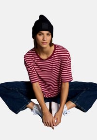 Striped maroon and pink t-shirt with a round neckline, paired with dark wide-leg denim jeans and white high-top sneakers. Black knit beanie.