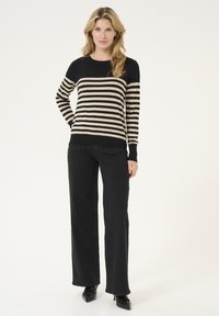 Pull rayé noir et beige avec un col rond, des manches longues et des poignets côtelés, associé à un pantalon large noir et des escarpins noirs à bouts pointus.