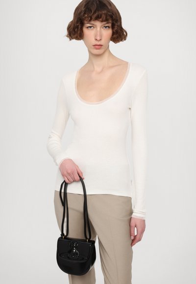 Long-sleeve white top with a scoop neckline, paired with beige pants. A small black handbag with a curved shape and strap is held in the hand.