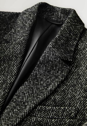 Marynarka w wzór houndstooth w czarno-białej wełnie, z wyciętymi klapami i jedną kieszenią, podszewką w gładkim czarnym kolorze.