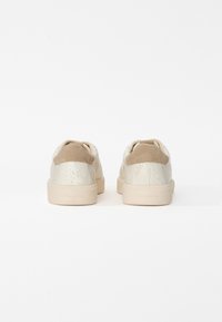 Paire de baskets basses beiges avec dessus texturé et détail en daim au talon, vue de dos sur fond blanc.
