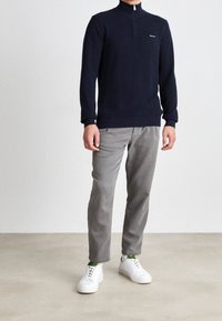 Navy zip-neck sweater with long sleeves, paired with gray pants and white sneakers. The sweater has a smooth texture and a fitted design.