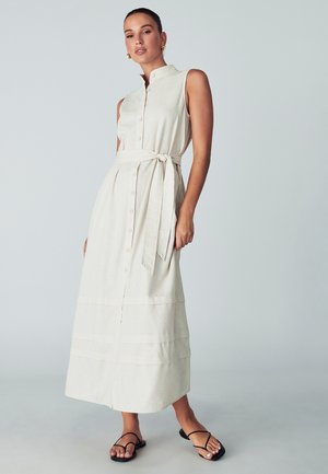 Beige linane maksikleit kõrge kaelusega, erinevate nuppudega esiosaga, vöökoht kinnitatud nööriga ja kihiline disain. Kombineeritud mustade lapikute sandaalidega.