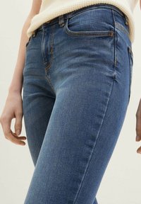 Džíny z denimu v středně modré barvě se slim fit, nabízející pět kapes, oranžové švy a hladkou texturu.