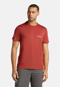 Rød kortærmet t-shirt lavet af blødt stof med rund hals, med et hvidt "icebreaker" logo på venstre bryst.