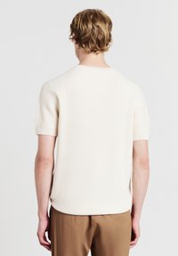 Maglione lavorato a maglia color crema a maniche corte con un motivo testurizzato, scollatura rotonda e orlo dritto. Realizzato in un materiale traspirante.