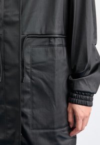 Schwarze, leichte Jacke mit strukturierter Oberfläche, ausgestattet mit einem Kordelzug in der Taille, elastischen Bündchen und einer Seitentasche.