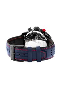 Montre-bracelet en acier inoxydable noir avec un cadran rond, un bracelet en cuir bleu marine, des surpiqûres rouges et des boutons-poussoirs proéminents. Fond de boîtier transparent.