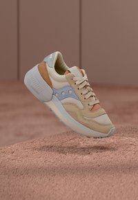 Beige sneakers featuring a mix of suede and mesh, with blue, orange, and tan accents, a textured sole, and a prominent logo on the tongue.