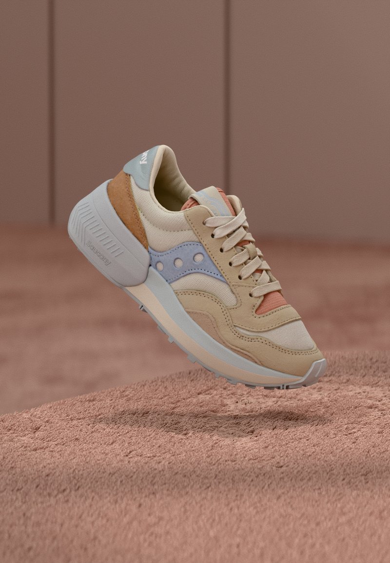 Beige sneakers featuring a mix of suede and mesh, with blue, orange, and tan accents, a textured sole, and a prominent logo on the tongue.