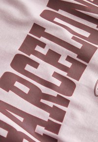 Tessuto grigio caratterizzato da grandi e audaci lettere color bordeaux. Il testo presenta un carattere robusto con una texture liscia e morbida su tutto il materiale.