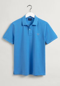 Polo bleu en coton, avec un col classique, trois boutons, et un petit logo brodé sur la poitrine gauche.