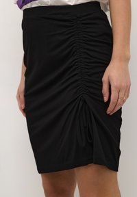 Jupe stretch noire avec détail froncé sur le côté et cordon de serrage. Matière douce, longueur genoux, design près du corps. Texture lisse.