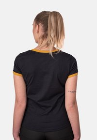 Camiseta negra de manga corta con un cuello y acentos en las mangas amarillos. Textura suave, diseño ajustado. La vista trasera muestra un tatuaje en el brazo.
