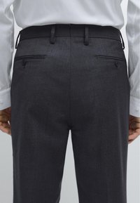 Mörkgrå skräddarsydda byxor med en jämn textur, med slät front, två bakfickor och bältesöglor, kompletterade med en vit skjorta.