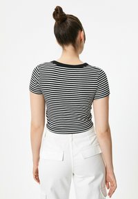 Camiseta de rayas negras y blancas de canalé con cuello redondo y mangas cortas, combinada con pantalones cargo blancos que tienen bolsillos traseros.