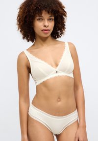 Σετ εσώρουχων με σουτιέν και σλιπ σε κρέμα χρώμα, με δαντελένιες λεπτομέρειες, μαλακό ύφασμα και κουμπί στο σουτιέν. Ο σχεδιασμός διαθέτει σχήμα V.