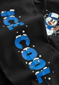 Černá tkanina zobrazuje velký, tučný modrý text "ICE COOL" s bílými sněhovými akcenty vedle barevné kreslené postavičky sněhuláka.