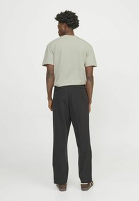 Hellgraues Baumwoll-T-Shirt und schwarze gerade geschnittene Hose. Das T-Shirt hat einen klassischen Rundhalsausschnitt; die Hose verfügt über Gesäßtaschen.